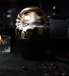 Goldener Daruma vor gusseiserner Teekanne und Kerze; Symbol für Erfolg & Fülle, handbemalt, 9 cm