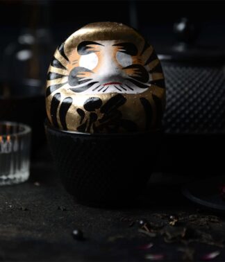 Goldener Daruma vor gusseiserner Teekanne und Kerze; Symbol für Erfolg & Fülle, handbemalt, 9 cm