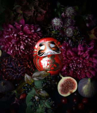 Roter Daruma zwischen dunklen Blumen, Beeren und Feigen; Symbol für Mut und Neustart, handbemalt, 9 cm