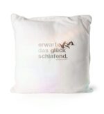 Weißes Kissen mit gesticktem Spruch „erwarte das glück schlafend.“