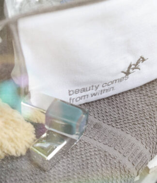 Nahaufnahme des gestickten Schriftzugs „beauty comes from within.“ auf weißem Beautycase
