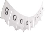 Weiße Stoffgirlande „Good Luck“ mit grauen Buchstaben in schräger Perspektive auf hellem Hintergrund
