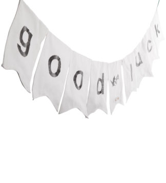 Weiße Stoffgirlande „Good Luck“ mit grauen Buchstaben in schräger Perspektive auf hellem Hintergrund