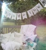 Good-Luck-Girlande über Gartenbank mit Kissen und dekoriertem Tisch in stimmungsvollem Outdoor-Arrangement