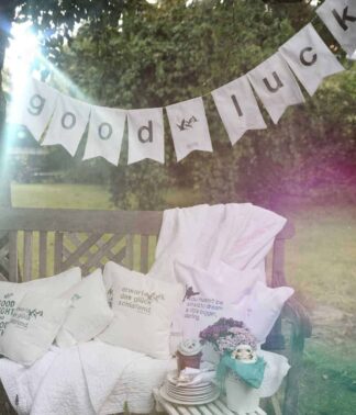 Good-Luck-Girlande über Gartenbank mit Kissen und dekoriertem Tisch in stimmungsvollem Outdoor-Arrangement