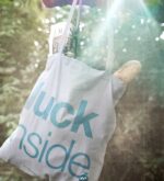 Grauer Jutebeutel mit petrolfarbenem Aufdruck „luck inside“ als Outdoor-Produktbild im Grünen
