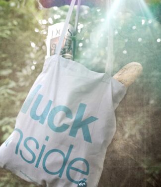 Grauer Jutebeutel mit petrolfarbenem Aufdruck „luck inside“ als Outdoor-Produktbild im Grünen