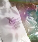 Weißes Kissen mit gesticktem englischem Spruch in heller Outdoor-Szene
