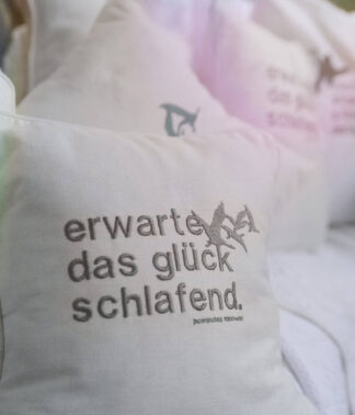 Weißes kleines Kissen mit gesticktem Spruch in ruhiger Outdoor-Szene