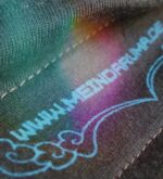 Makroaufnahme des meindaruma Logos unter dem Kragen auf braunem Tiger-Shirt