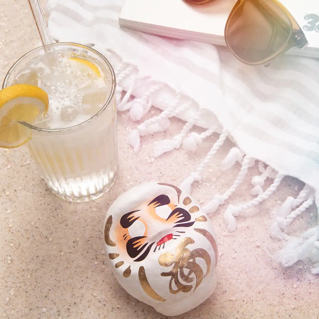 Weißer Daruma auf Sand am Strand, Symbol für Klarheit und Fokus, 9 cm