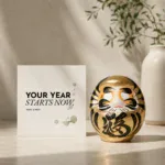 Grußkarte „YOUR YEAR STARTS NOW“ neben goldenem Daruma in ruhiger Produktinszenierung