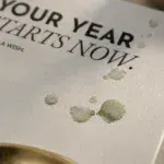 Detail der Grußkarte „YOUR YEAR STARTS NOW“ mit Aquarellflecken und glänzendem Acryllack auf cremefarbenem Naturpapier