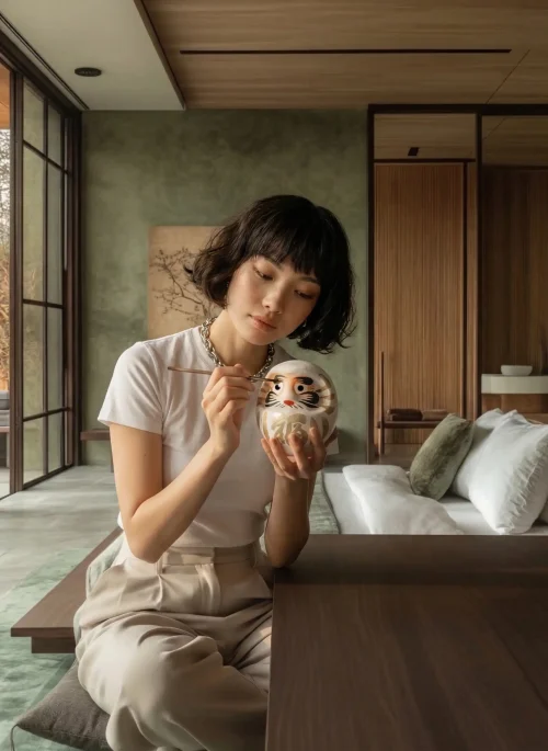 Frau malt das Auge eines weiß-goldenen Daruma aus